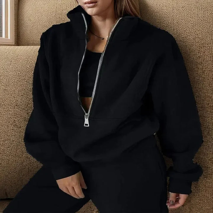 Une femme porte un ensemble noir décontracté avec un haut à col zippé et un pantalon assorti. Ce look élégant et confortable est idéal pour les journées fraîches d'hiver.